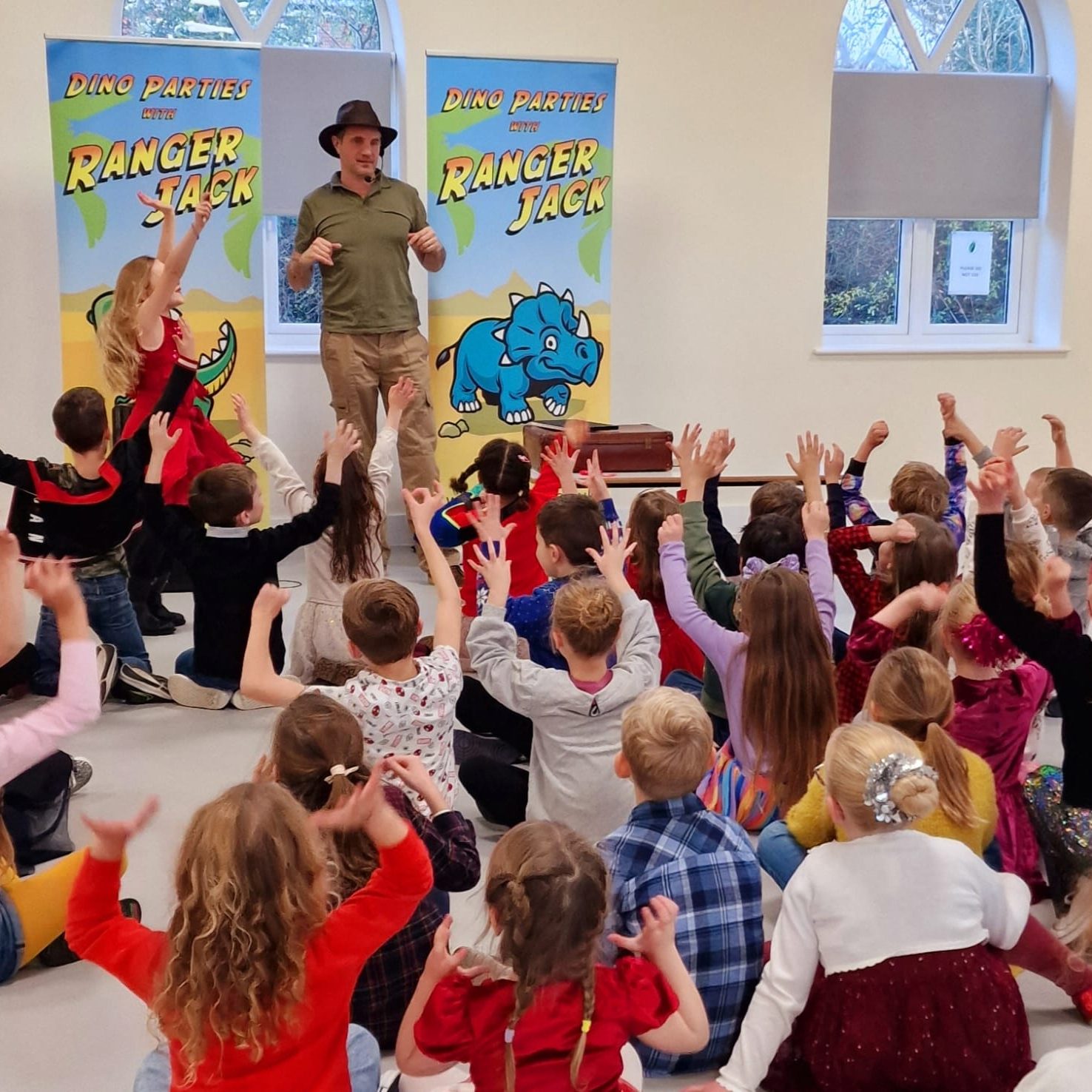 Happy children lifting their arms whilst taking part in a Dino Party with Ranger Jack